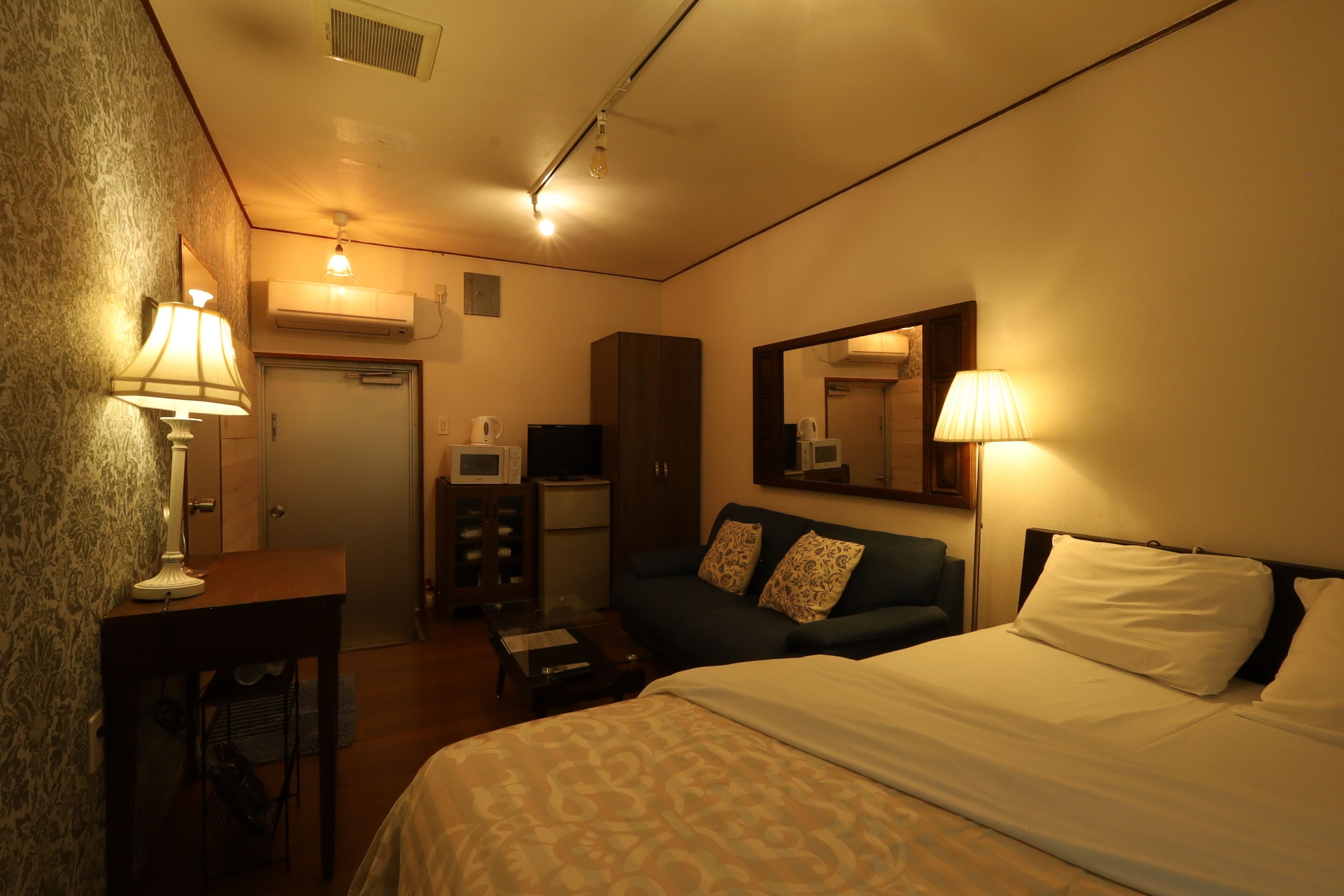 A hotel room with a bed, a desk, a chair, a dresser, and a mirror.