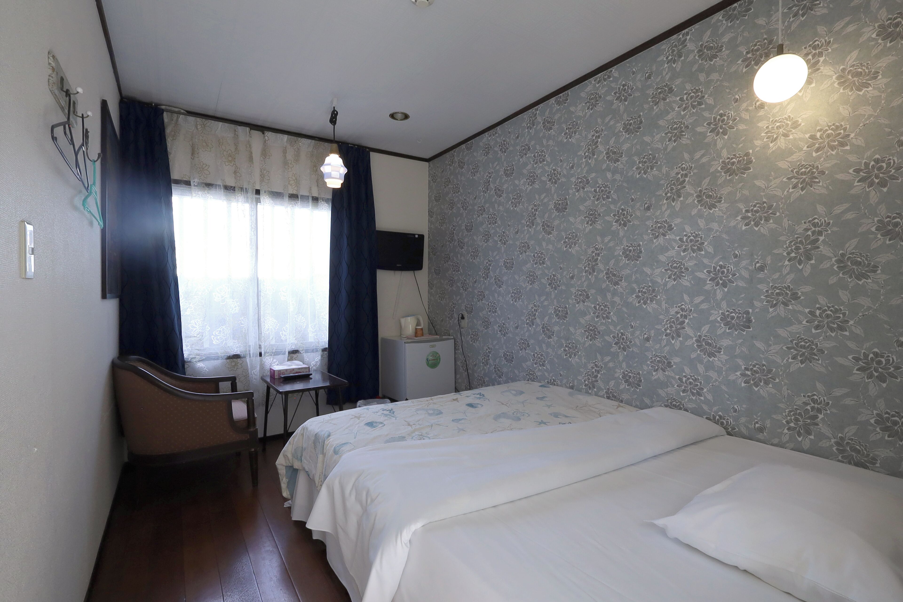 A hotel room with a bed, a desk, a chair, a small refrigerator, and a window with curtains.