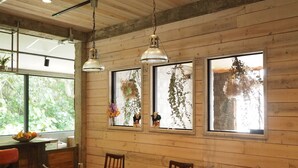Comedor con paredes de madera, ventanas amplias con plantas y lámparas colgantes.