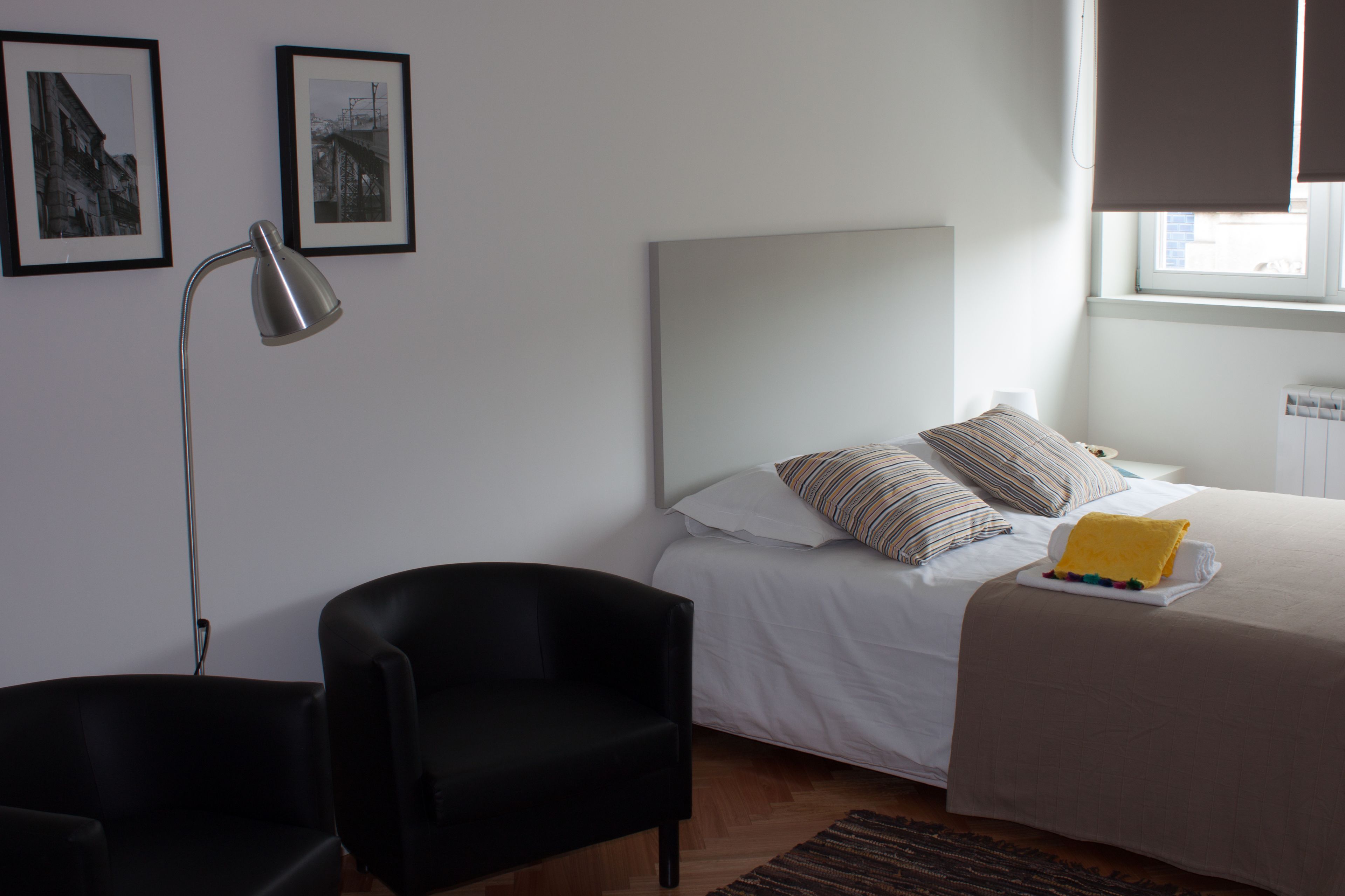 A bedroom with a bed, a black chair, a desk lamp, and two framed pictures on the wall.