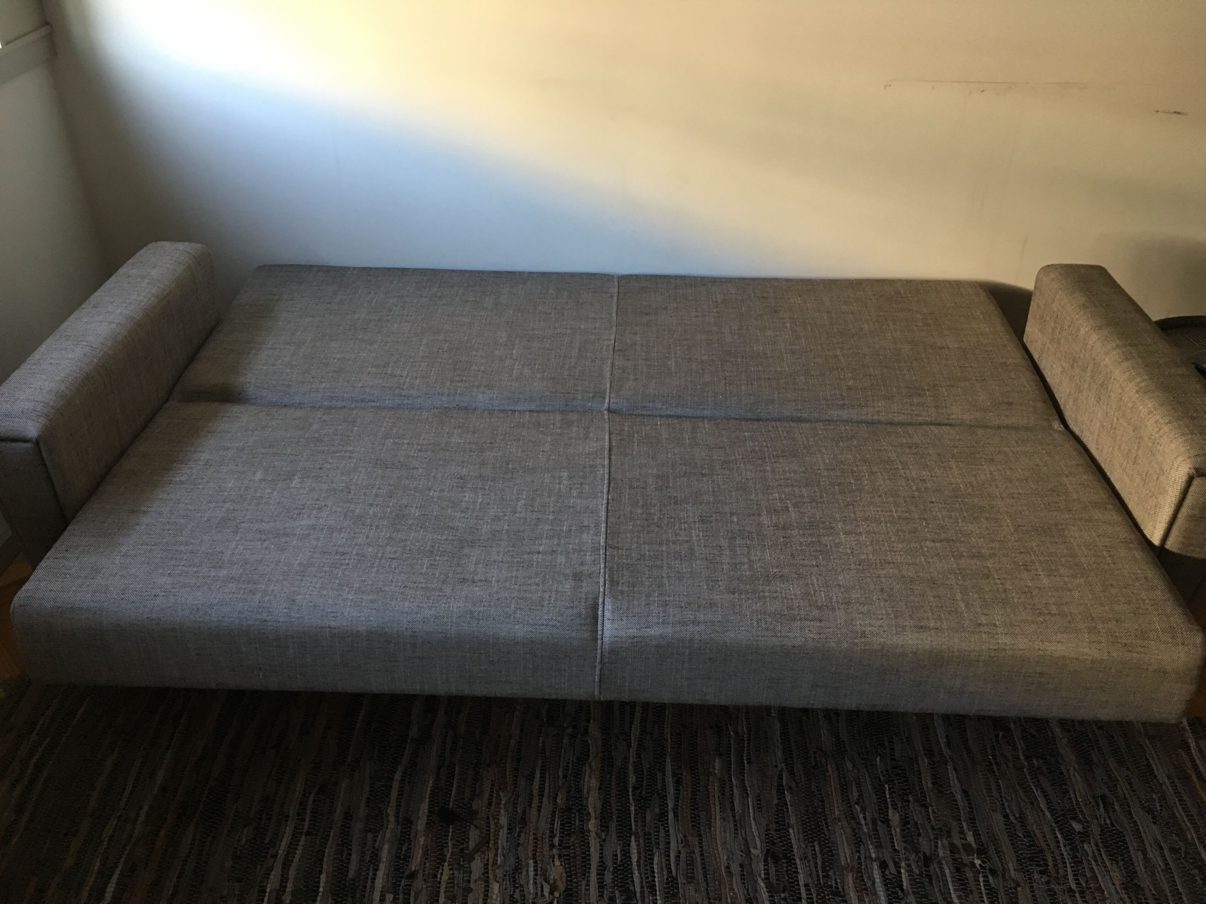 A grey sofa with a dark striped carpet in a room with white walls.