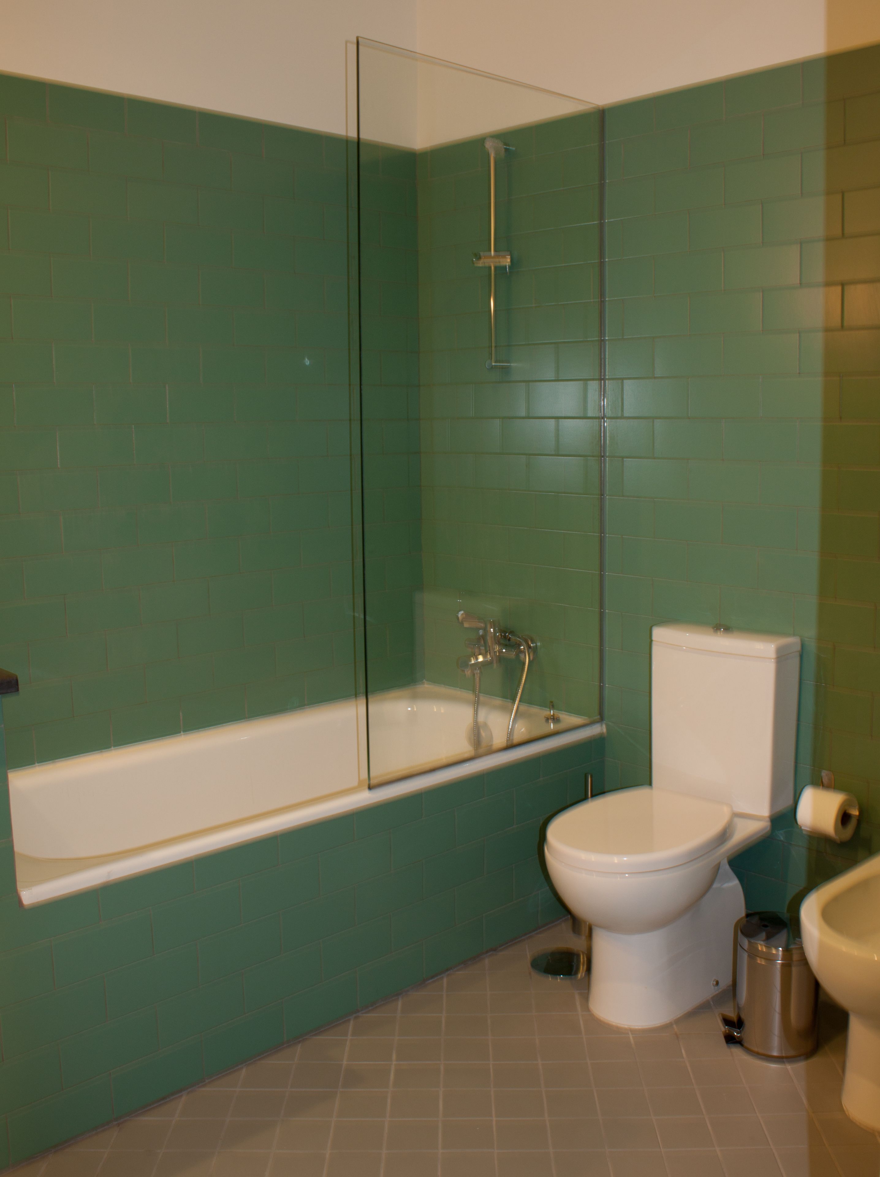 A bathroom with a glass-enclosed bathtub, a toilet, and a trash can.