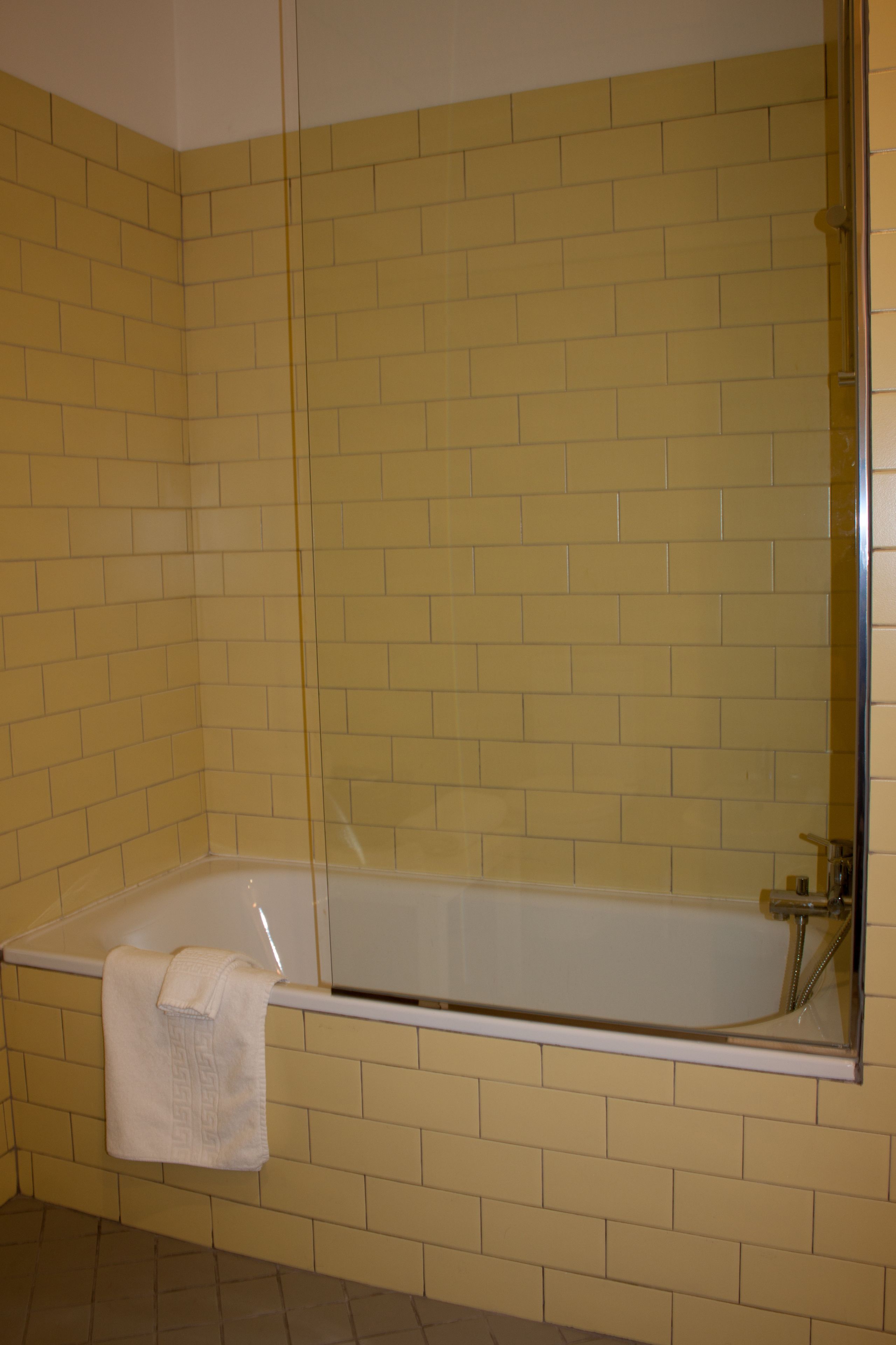 A bathroom with yellow tiled walls, a white bathtub, and a glass shower enclosure.