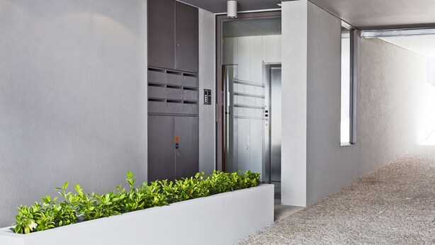 A modern hallway with a concrete floor, a white planter with green plants, and a glass elevator door. - bnapartments Palacio (Porto)