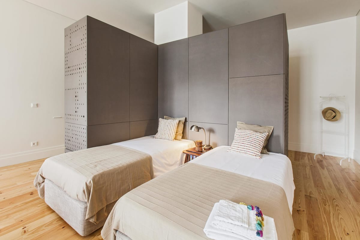 Una habitación de hotel moderna con dos camas, un armario grande y suelo de madera.