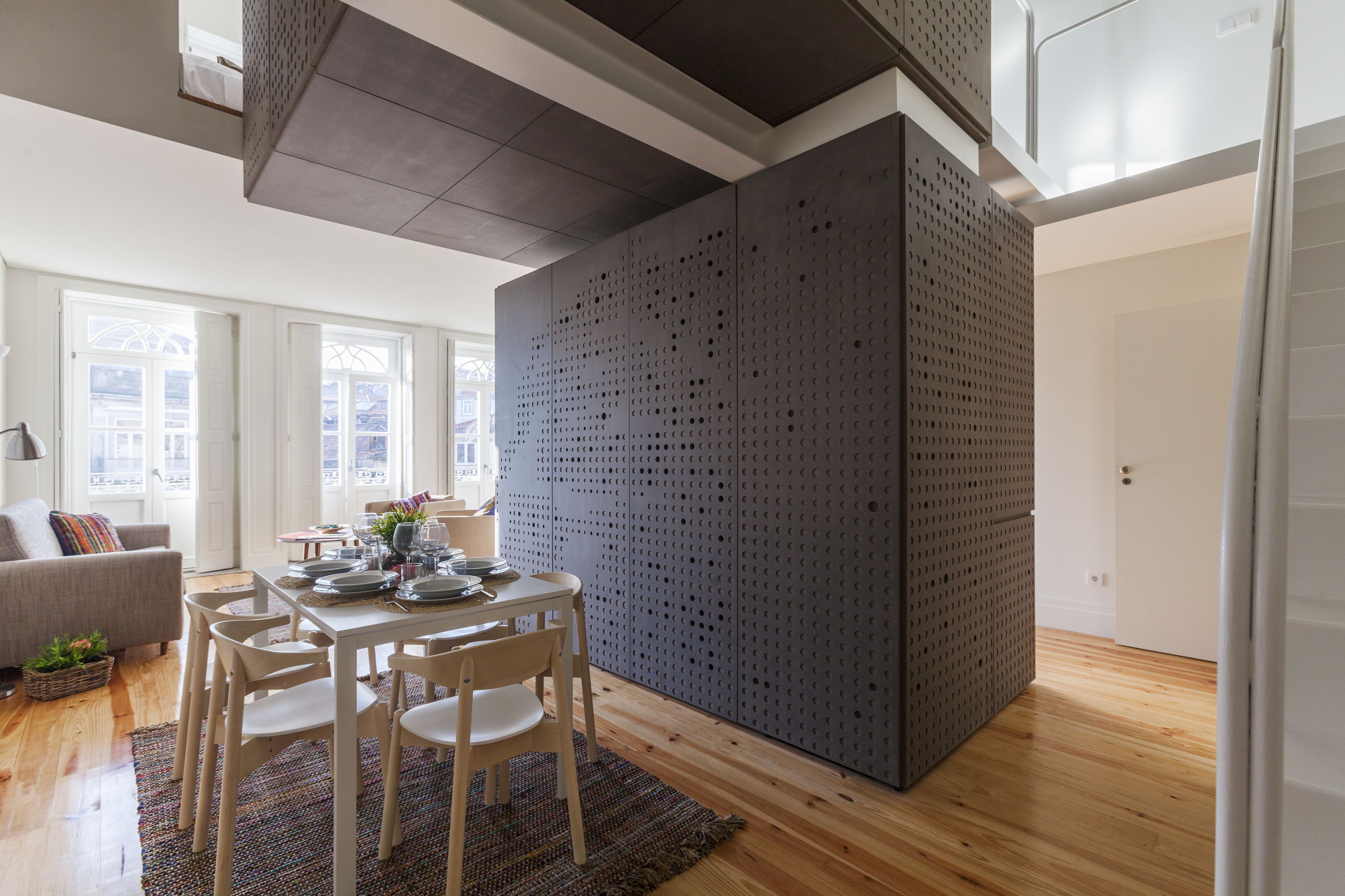 A modern dining area with a high ceiling, a grey perforated partition, and a wooden dining table set for four.