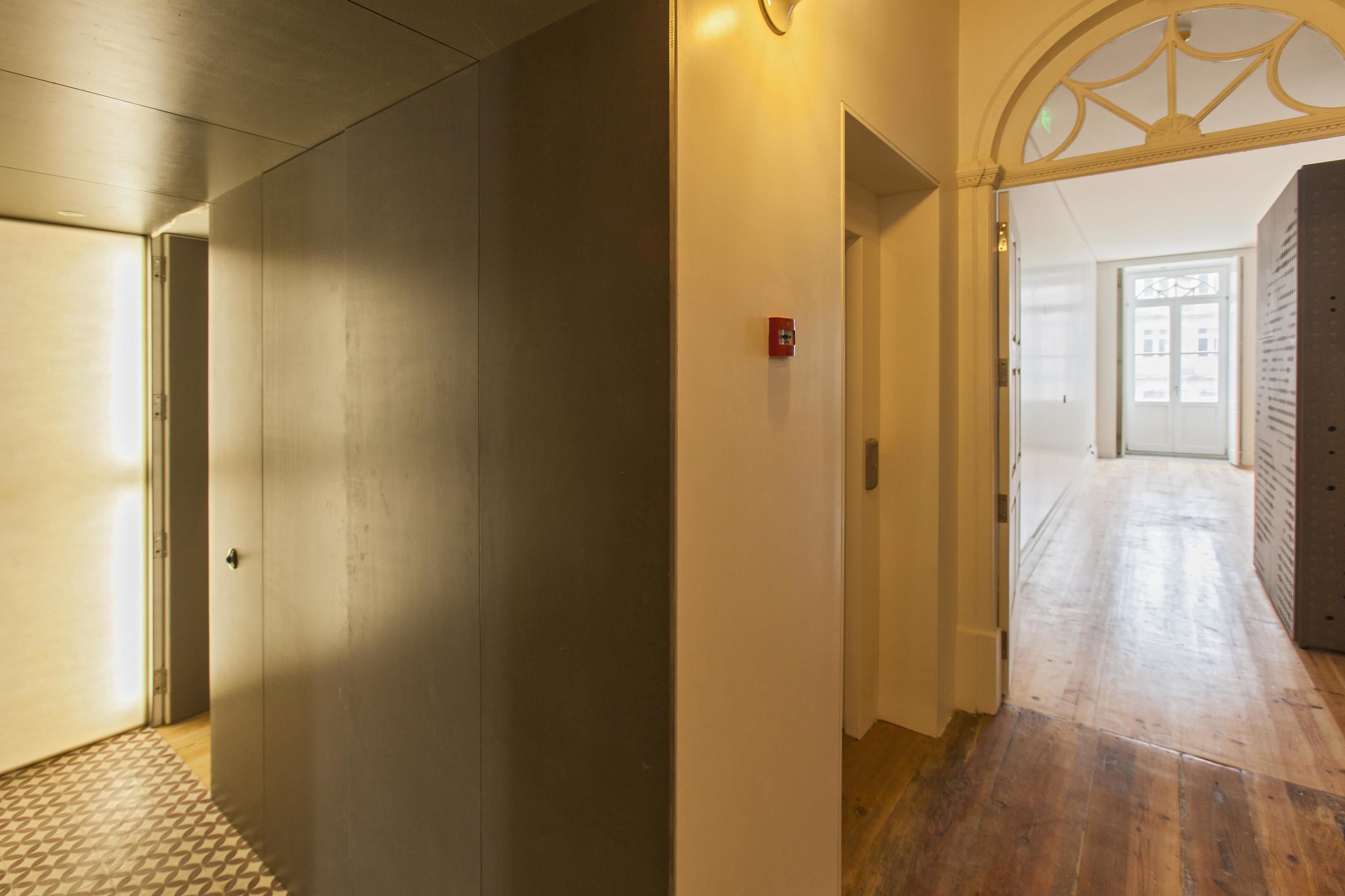 Een gang met een houten vloer, een kamerbreed tapijt met patroon en een deur naar een andere kamer.