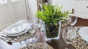 Een eettafel gedekt met glazen servies, borden en een potplant.