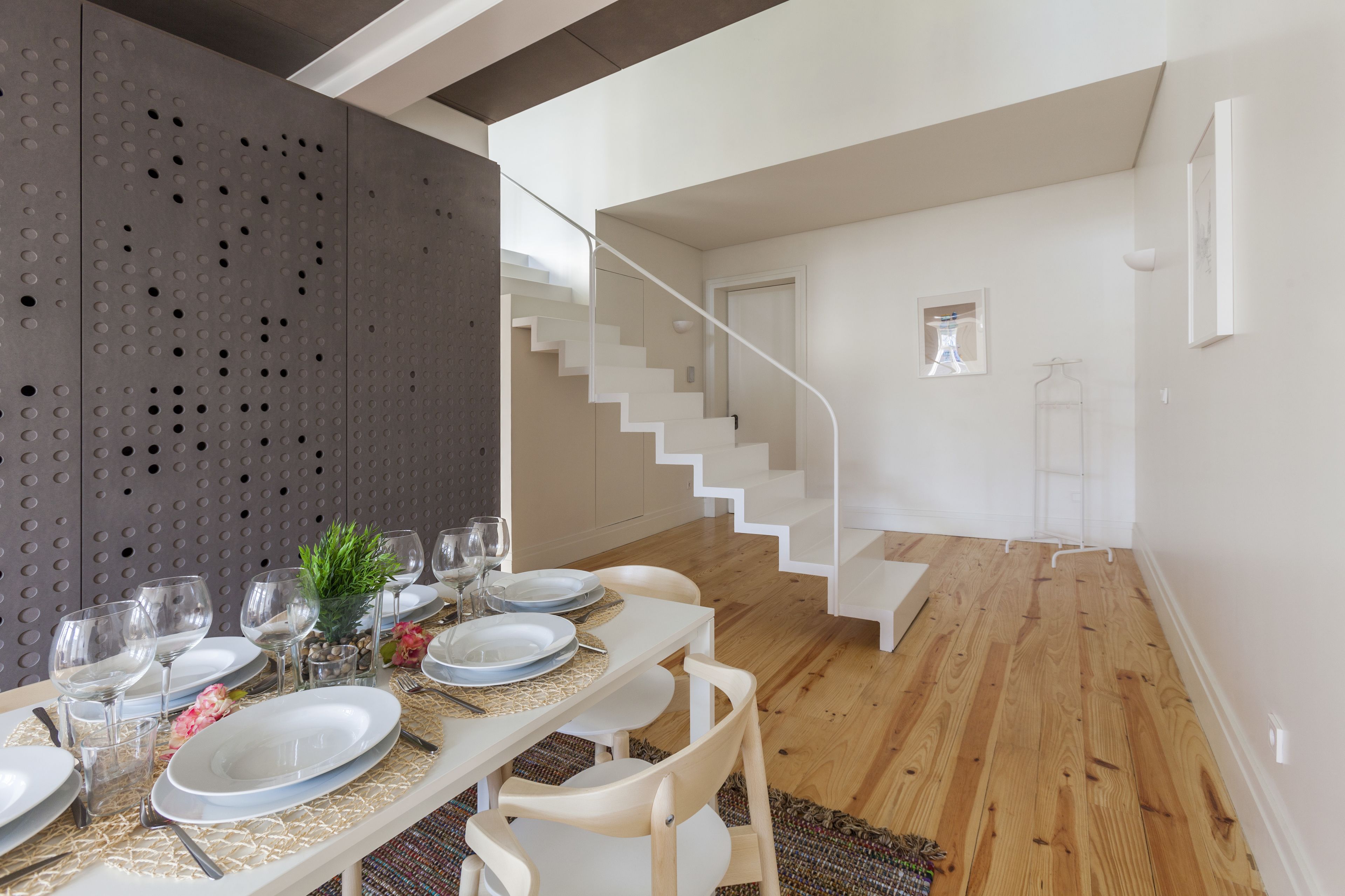 A dining area with a table set for six, a staircase, and a view of a hallway.