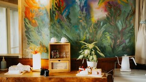 A wooden table with a white teapot, cups, and a potted plant. A colorful abstract painting is on the wall behind. - BUZZ RESORT (Onna)