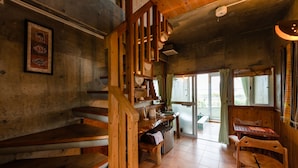 A rustic wooden interior with a staircase, wooden benches, a small table, and a view of the outdoors through large windows. - BUZZ RESORT (Onna)