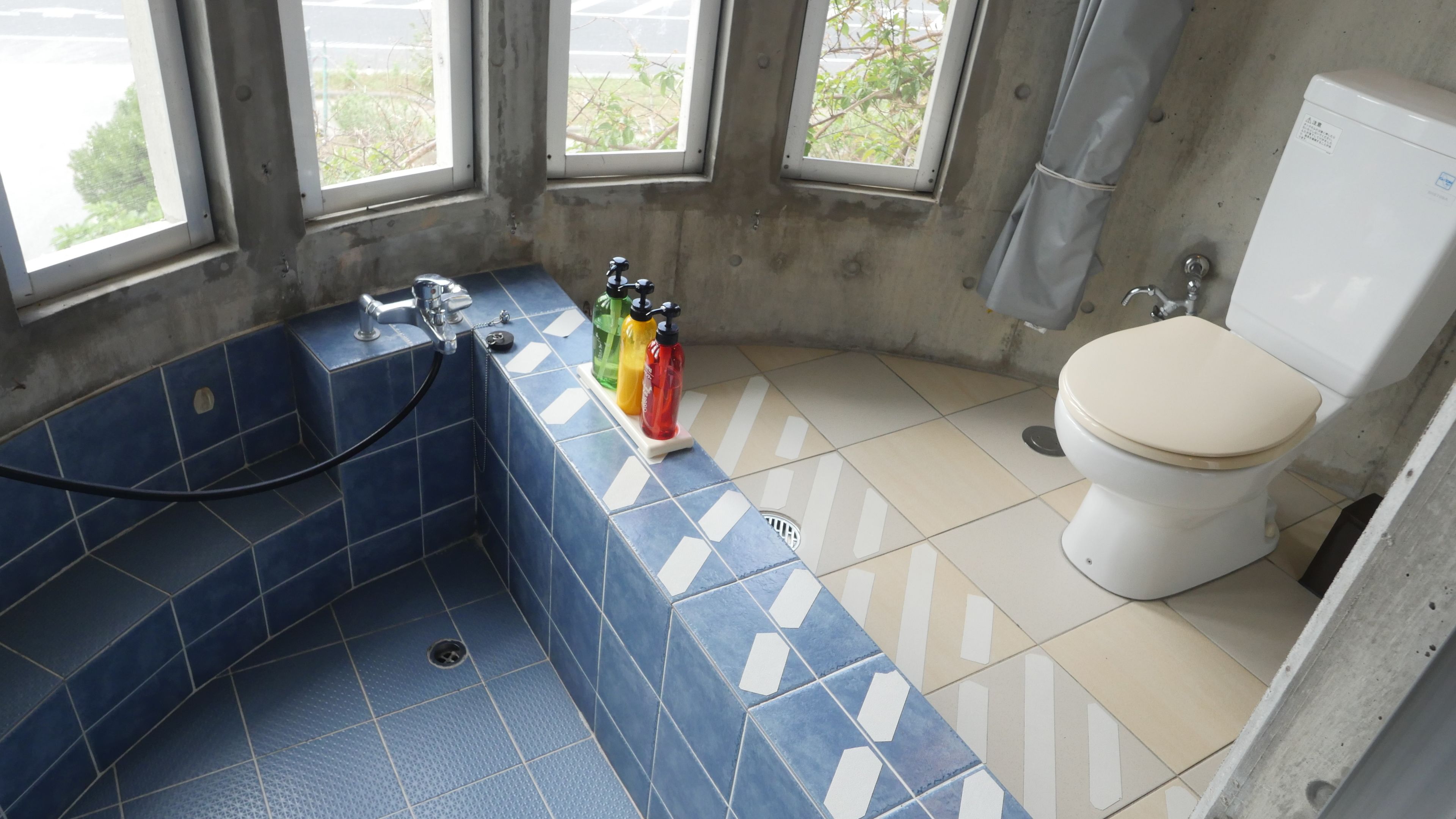 Un baño con ducha, inodoro y ventanas.