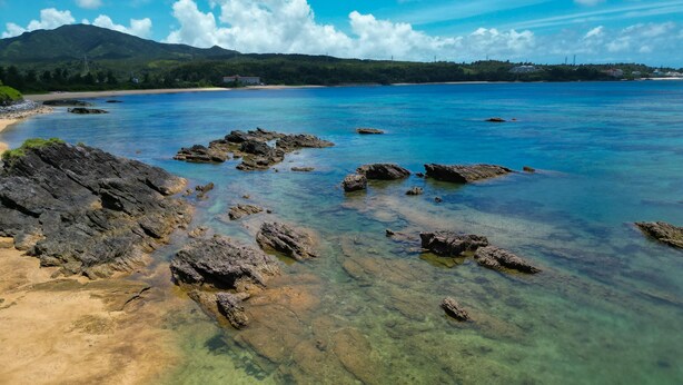 A coastal landscape with clear waters, rocky outcrops, and a distant mountain range. - BUZZ RESORT (Onna)