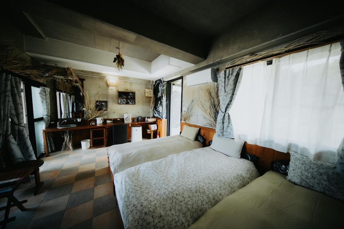 A room with two beds, a desk, and a window with curtains.