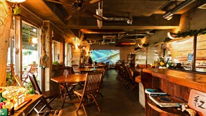 A restaurant interior with wooden tables and chairs, a bar area, and a projection screen displaying a blue image. - BUZZ RESORT (Onna)