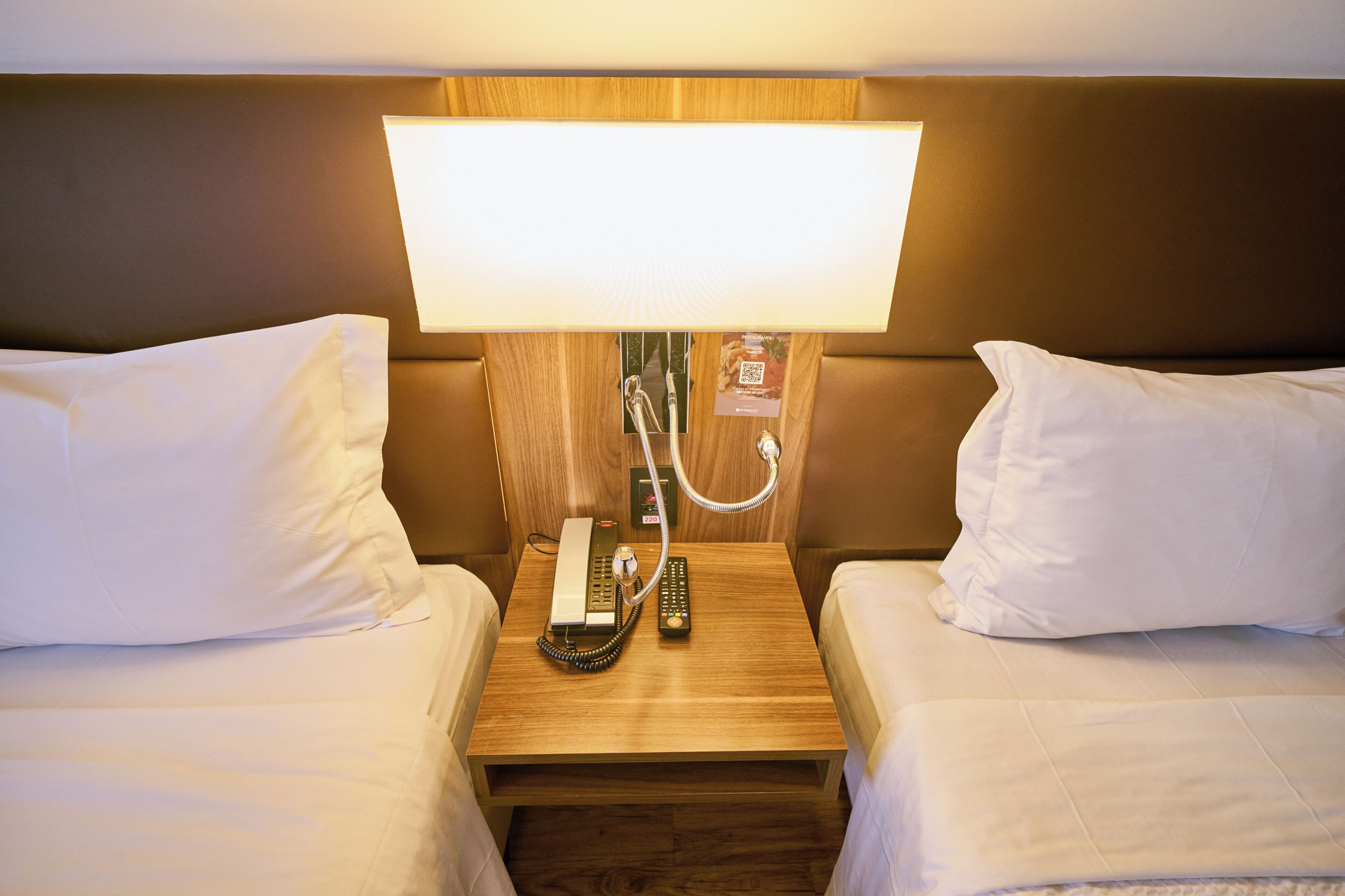 Une chambre d’hôtel avec deux lits, une table de chevet avec une lampe, un téléphone et une télécommande.