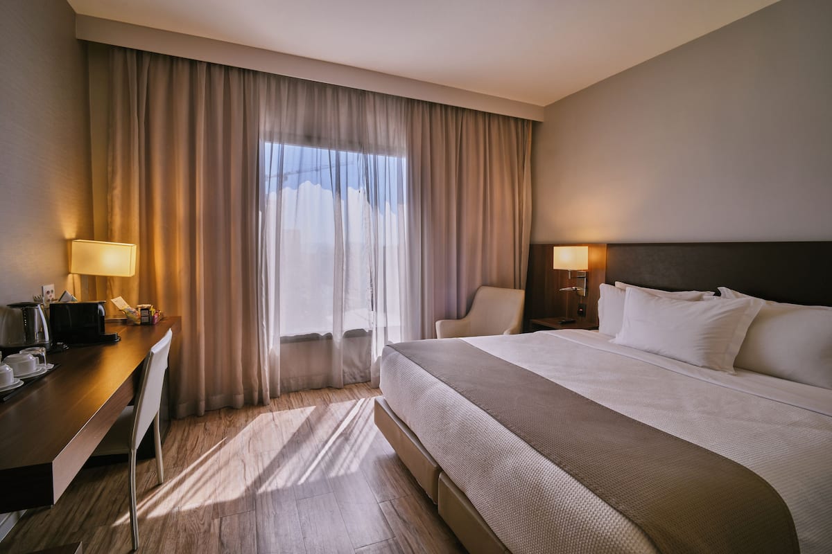 A hotel room with a bed, desk, chair, lamps, and curtains.