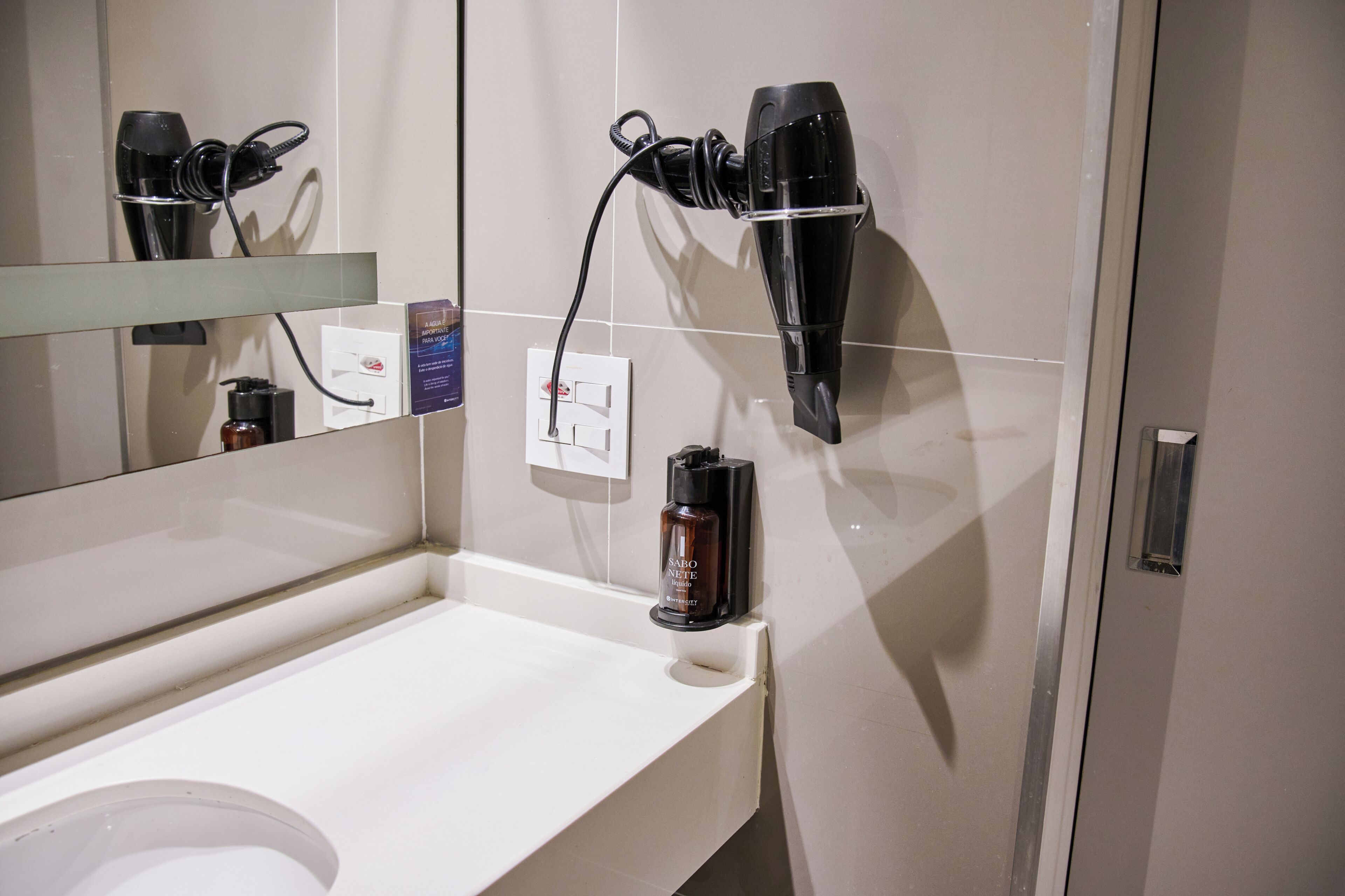 A bathroom with a mirror, a hairdryer, a bottle, and a towel rack.