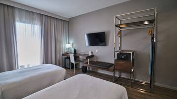 Habitación de hotel con dos camas, un escritorio con silla, televisor, perchero y caja fuerte.