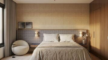 Quarto com uma cama grande, duas mesas de cabeceira, uma cadeira redonda, luminária fixada na parede e guarda-roupa de madeira.
