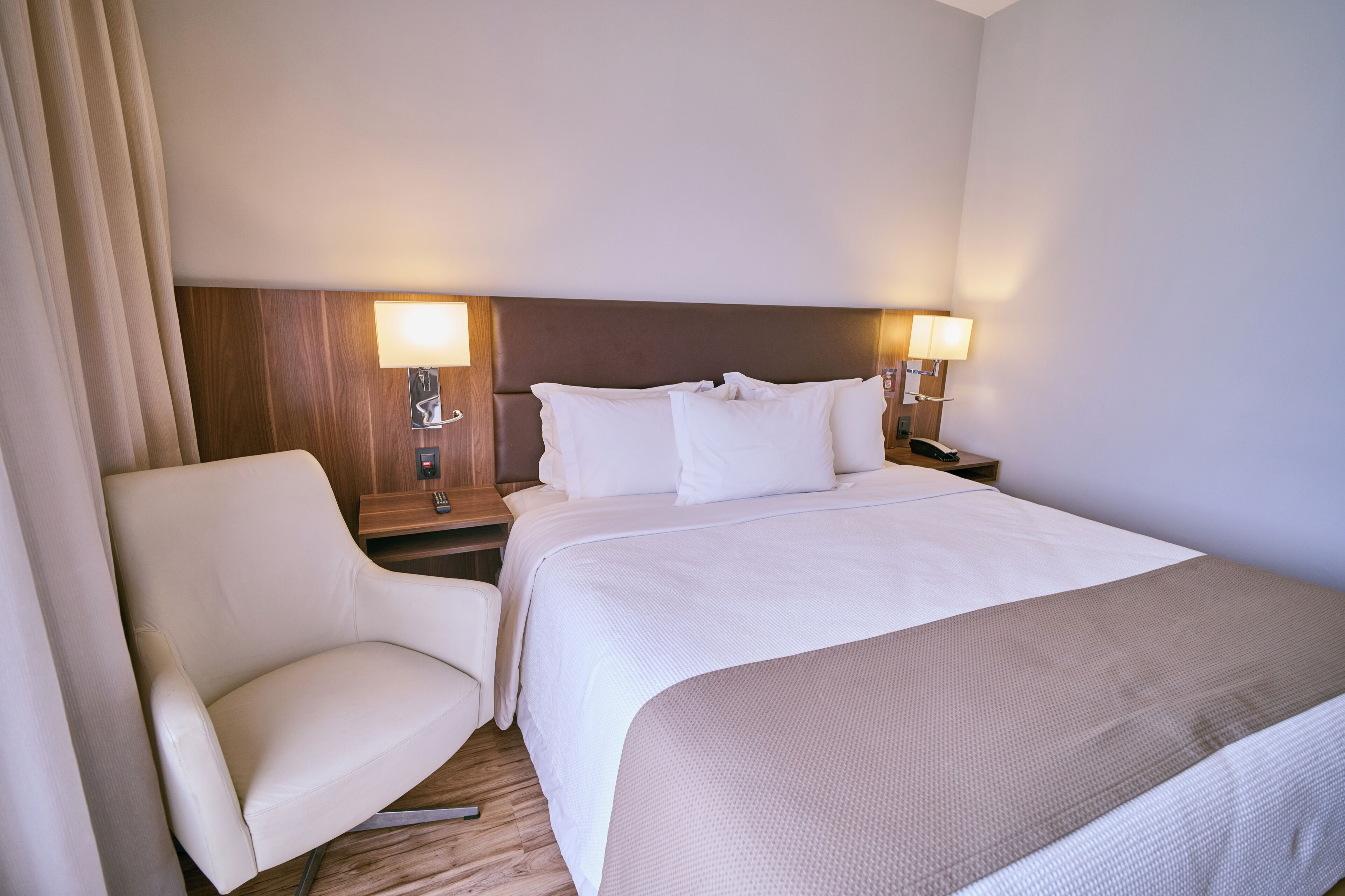 A hotel room with a bed, two bedside tables, a chair, and a lamp.