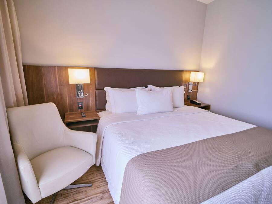 A hotel room with a bed, two bedside tables, a chair, and a lamp.