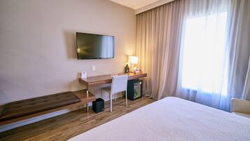 A hotel room with a bed, a desk with a chair, a television, a lamp, and a window with curtains.