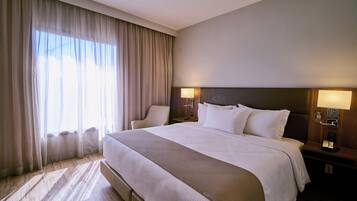 A hotel room with a large bed, two bedside lamps, a chair, and a window with curtains.