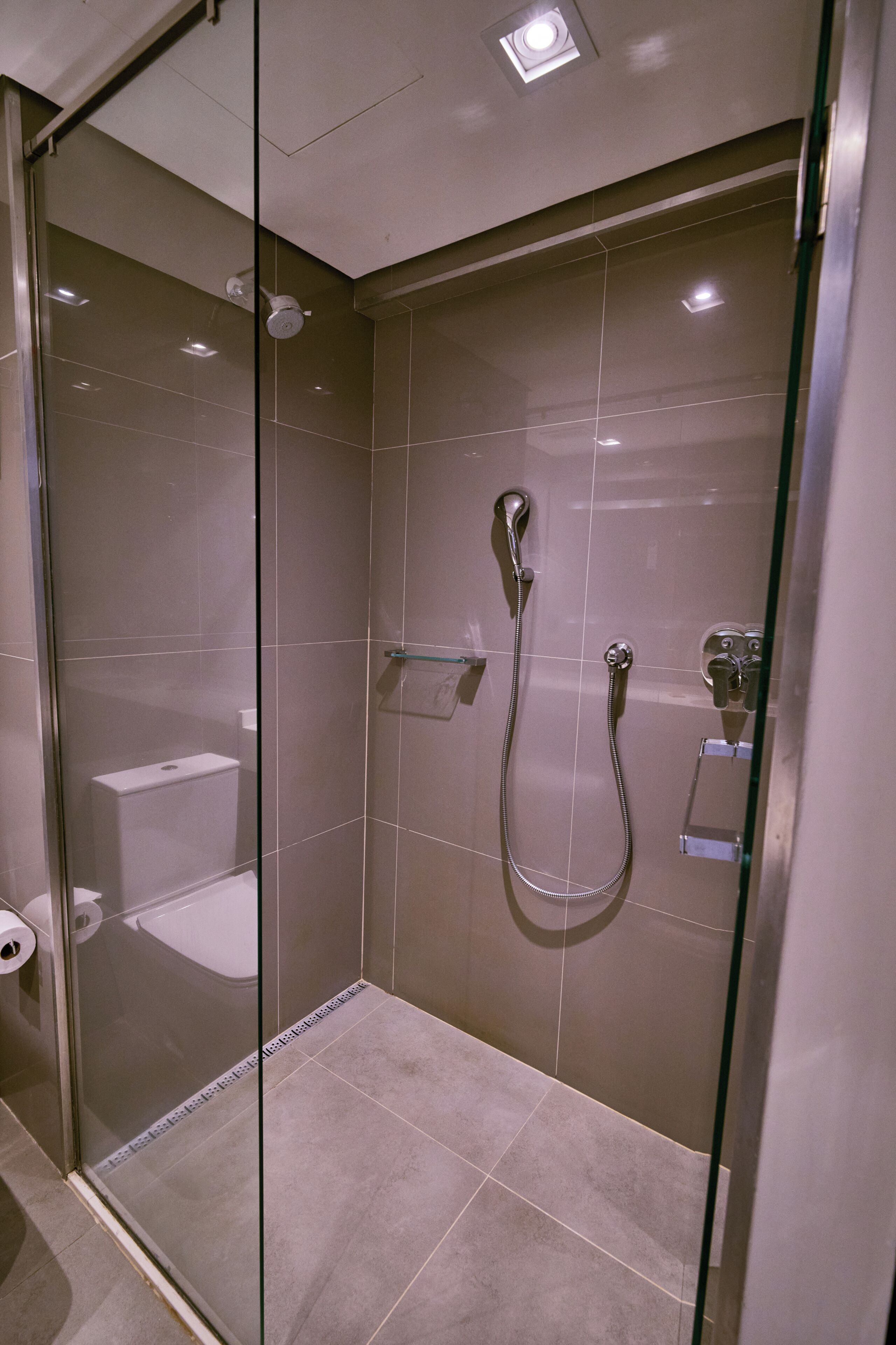 A glass-enclosed shower with a handheld showerhead and a wall-mounted faucet.