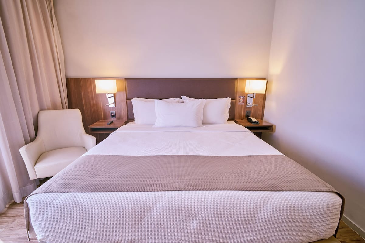 A hotel room with a large bed, two bedside tables, a chair, and a curtain.