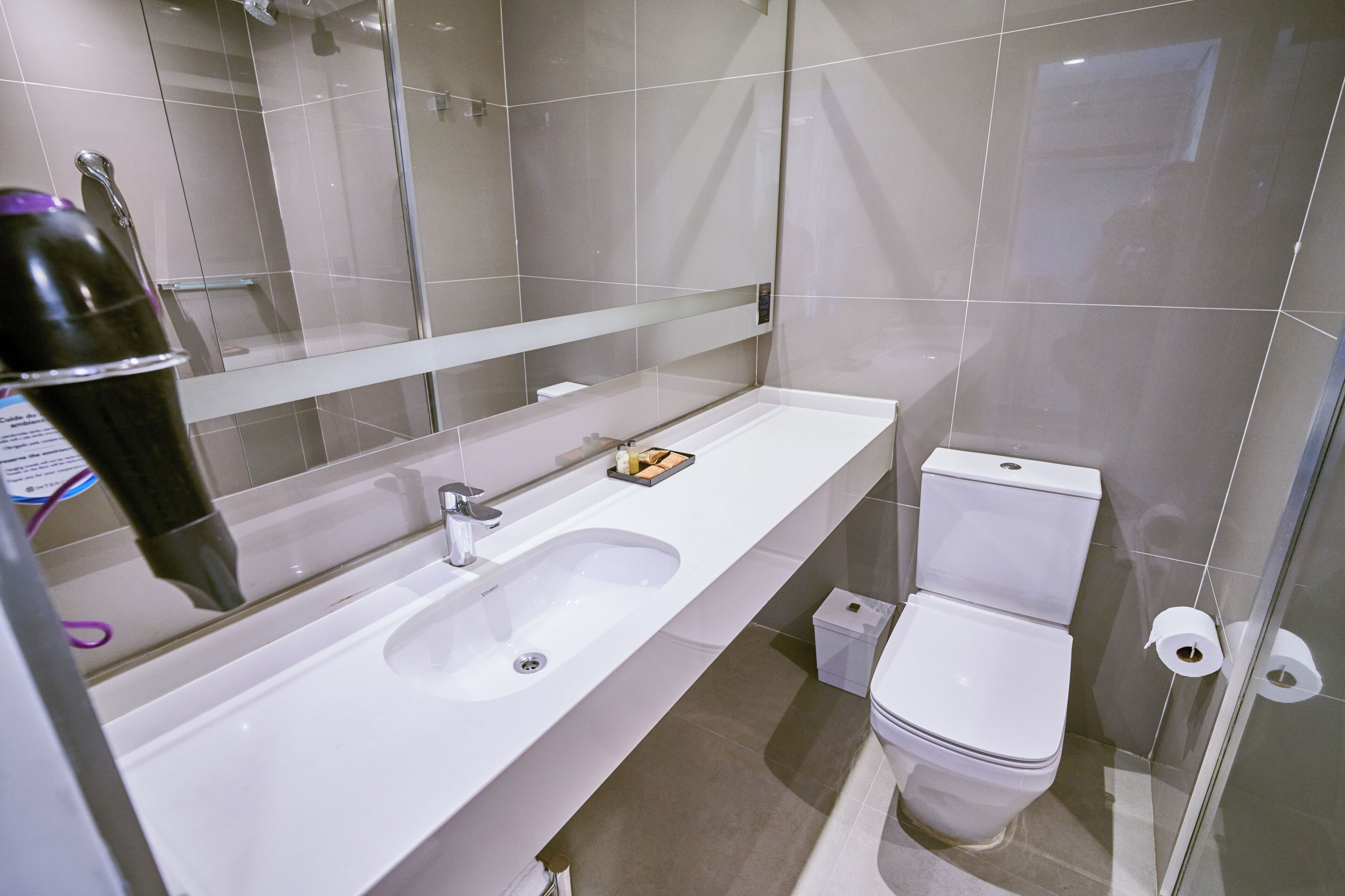 Un baño moderno con lavamanos, espejo y retrete blancos.