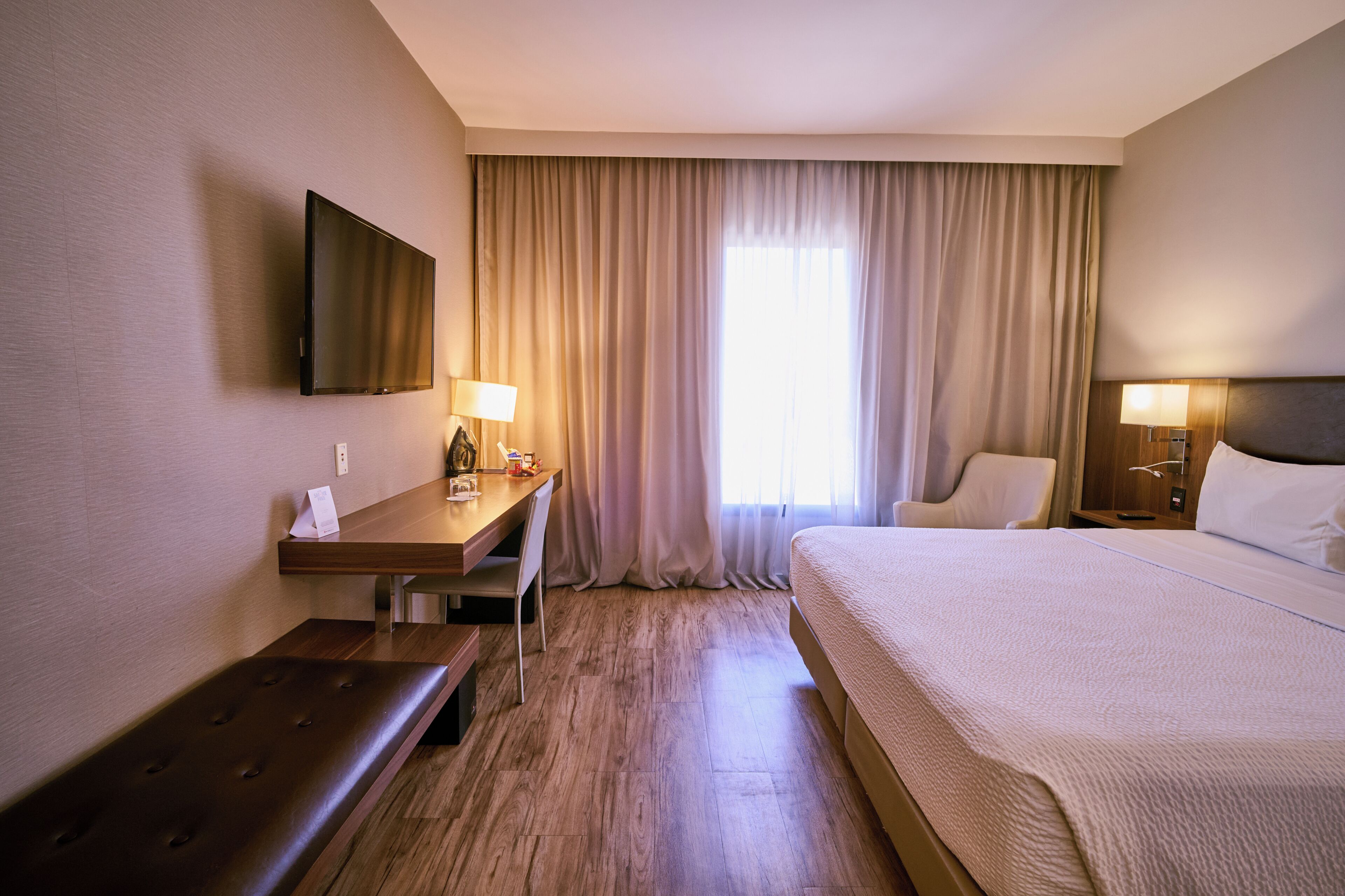 Habitació d'hotel amb llit, escriptori, cadira, televisió i finestra amb cortines.