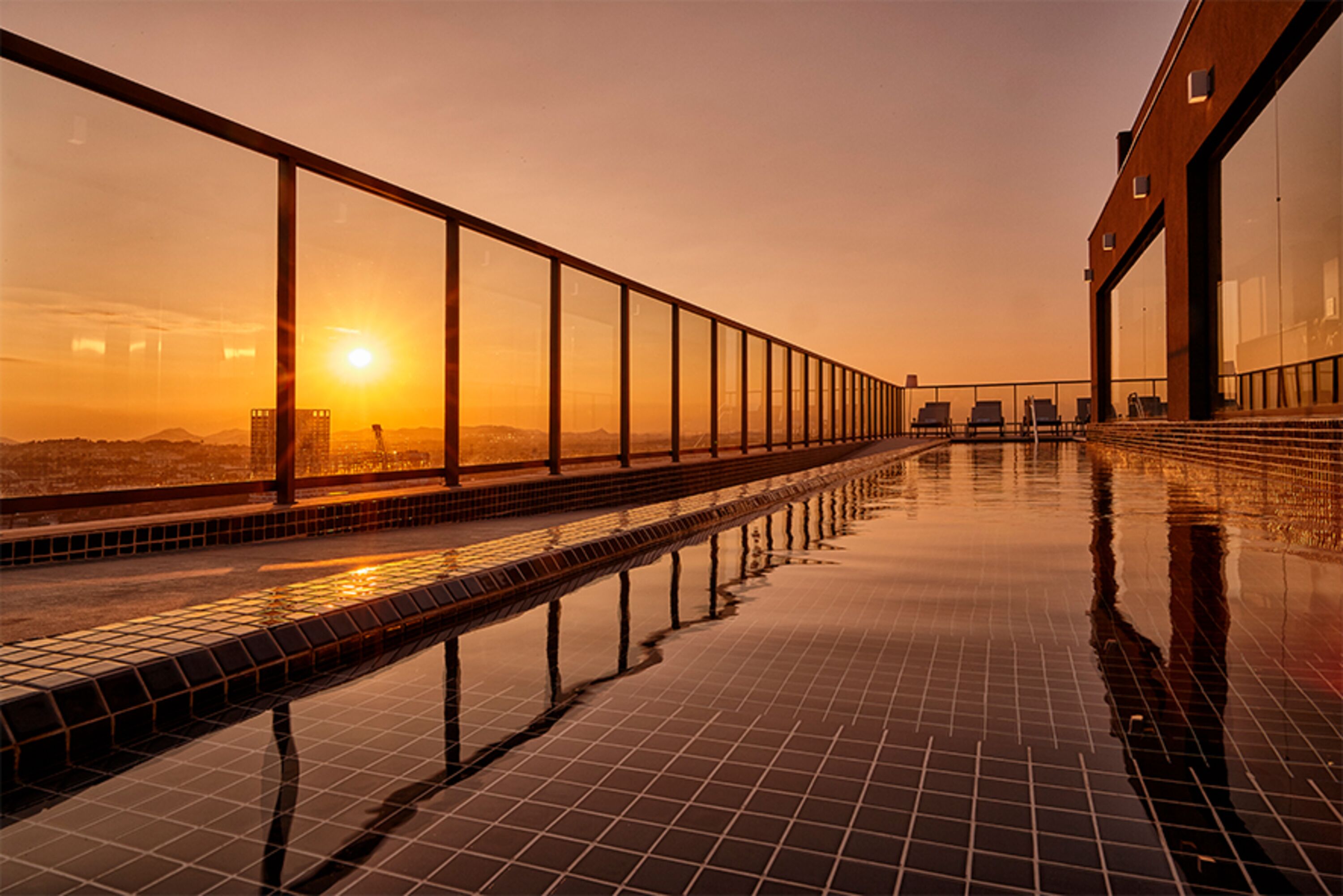A rooftop pool with a glass balustrade, reflecting the sunset.