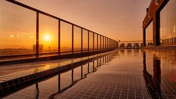 A rooftop pool with a glass balustrade, reflecting the sunset.
