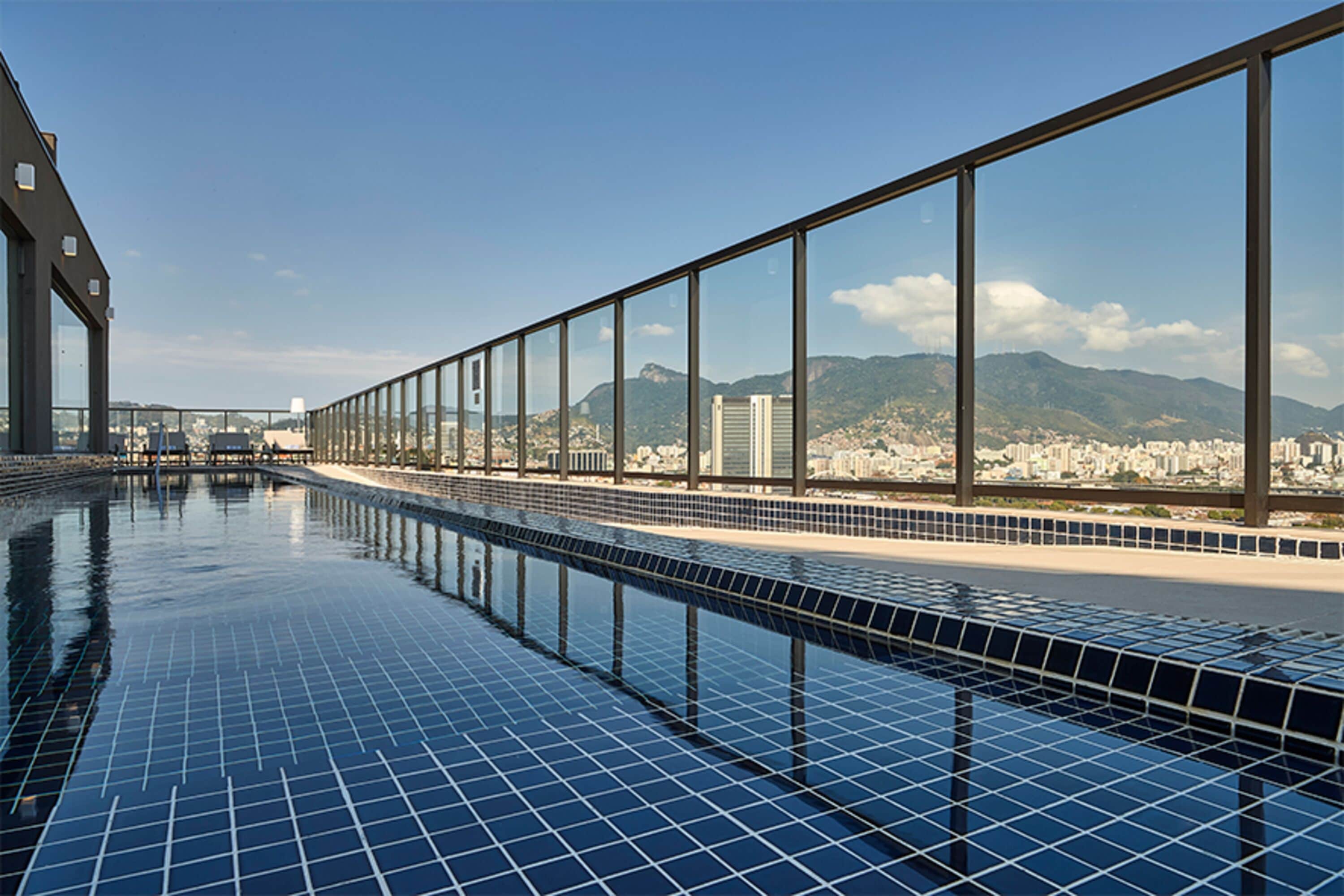 A long, narrow swimming pool with clear blue tiles and a view of a cityscape and mountains in the background.