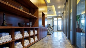Een hotel lobby met houten planken met handdoeken, een vaas en een kom. Achtergrond bevat fitnessapparatuur.