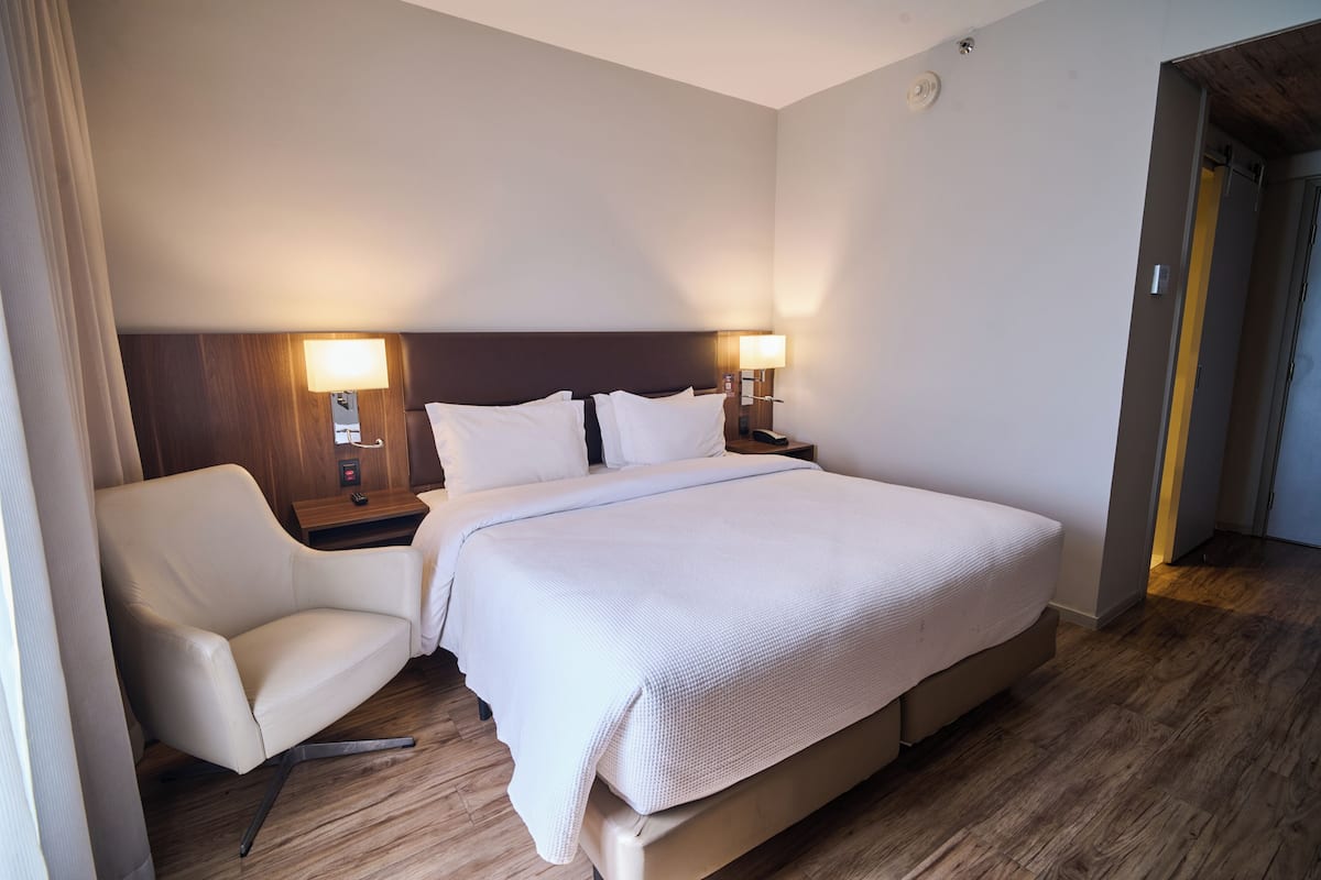 A hotel room with a bed, a chair, a nightstand, and a lamp.