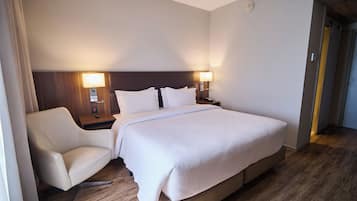 A hotel room with a bed, a chair, a nightstand, and a lamp.