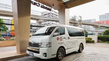 A white van parked under an overpass with signage for 'Best Western PLUS' and 'Wanda Grand Hotel.'