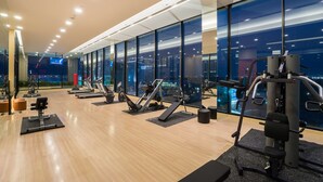 Uma academia moderna com diversos equipamentos de ginástica, grandes janelas e vista para a cidade.