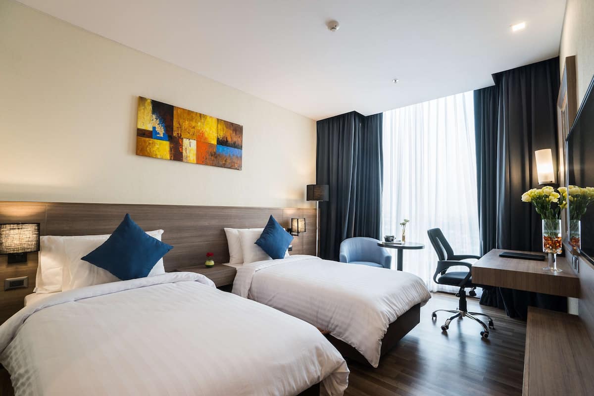 Une chambre d’hôtel avec deux lits, un bureau, une chaise et un tableau au mur.