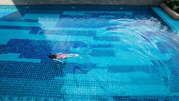 Una piscina con suelo de azulejos y una persona nadando.