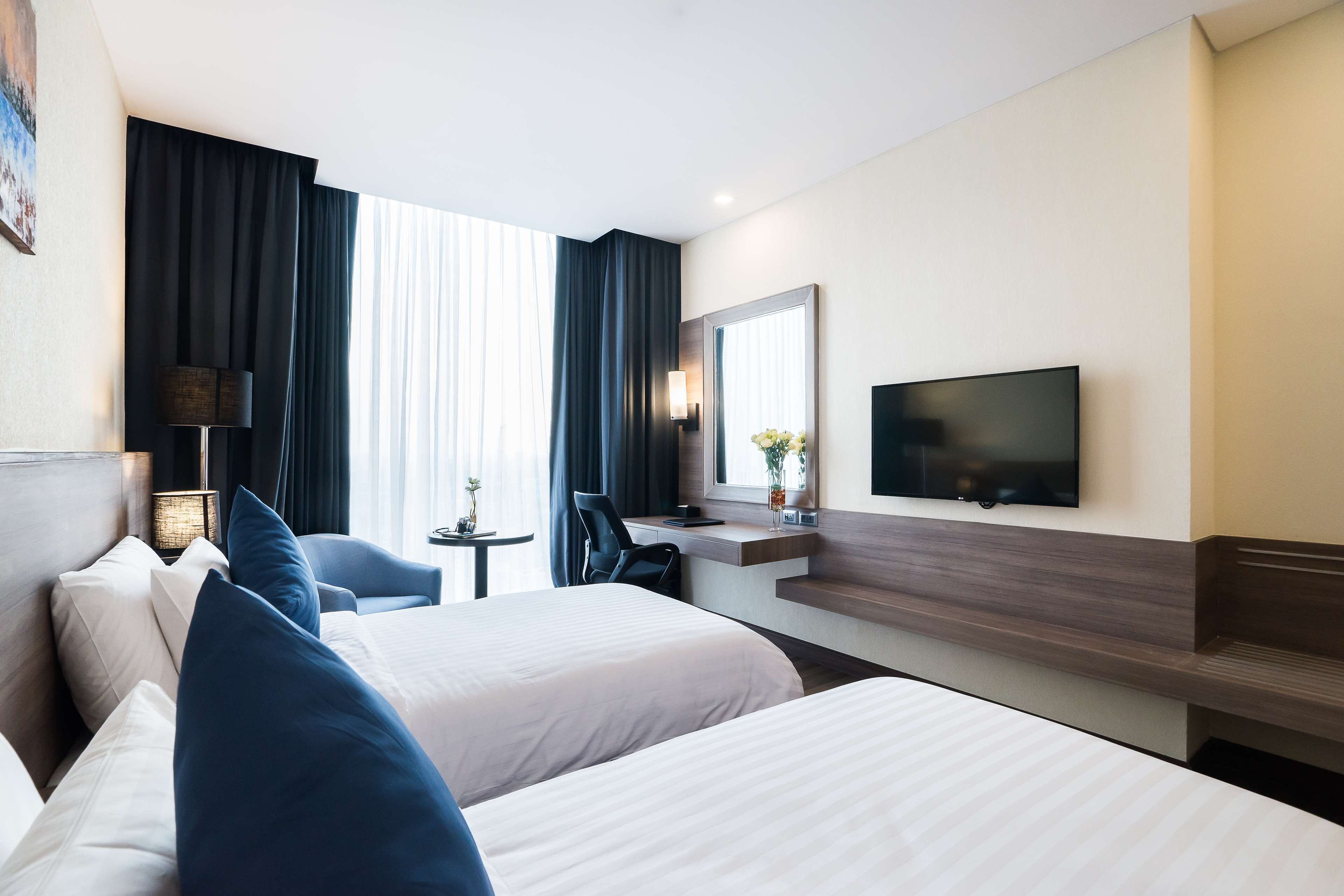 A hotel room with two beds, a desk, a chair, a TV, and a window with curtains.