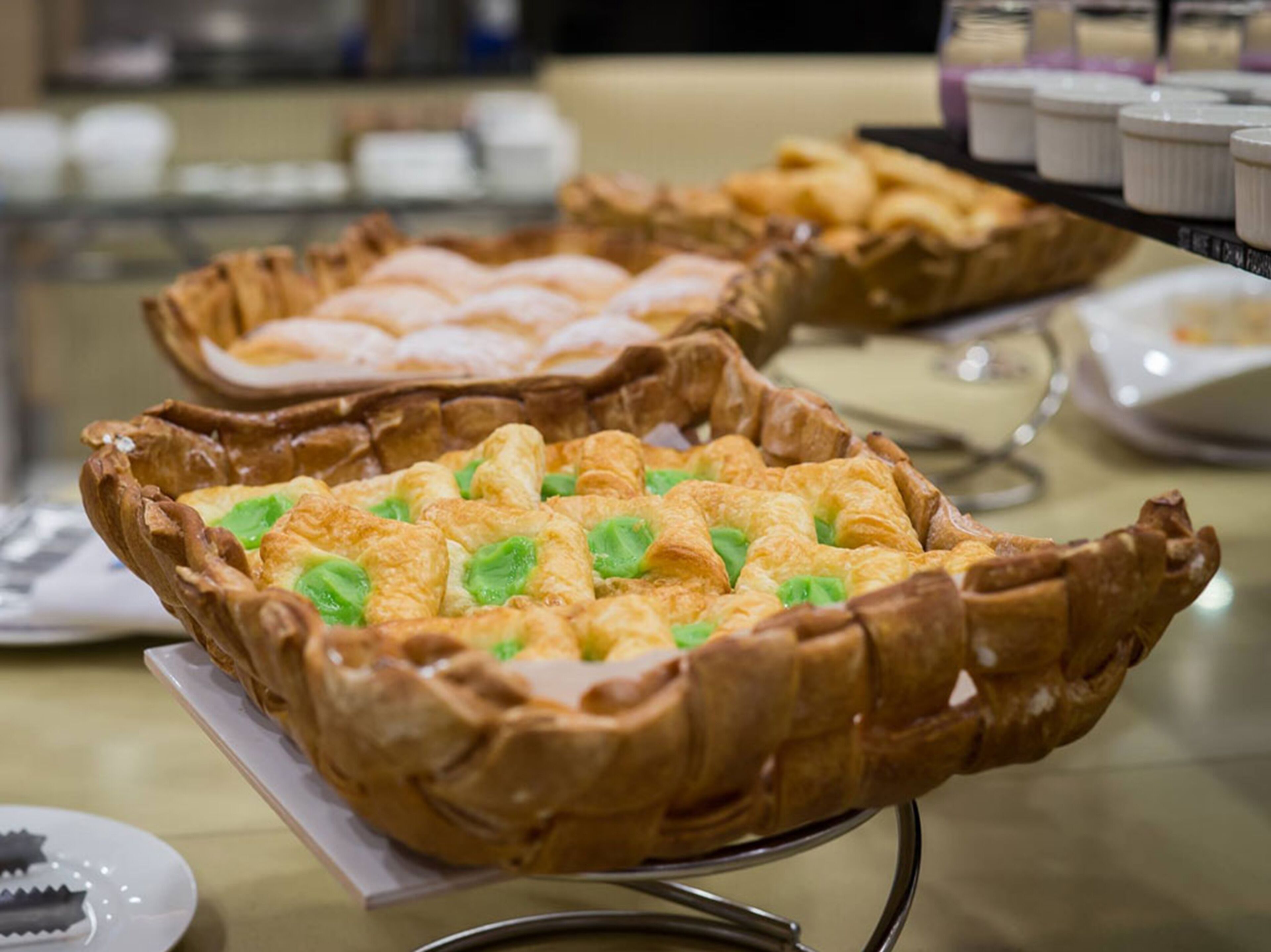 A buffet with various baked goods, including pies and pastries, displayed on a metal stand.