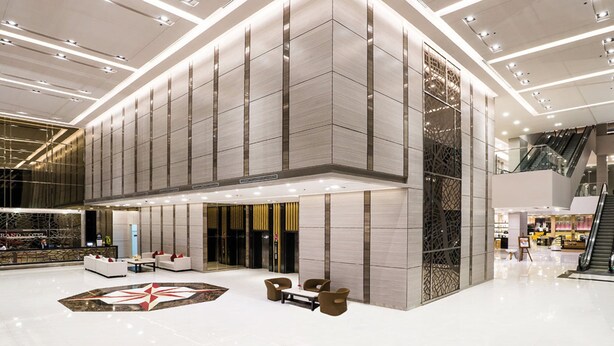 Um hall amplo com design moderno, apresentando uma área de estar central, um padrão de piso decorativo grande e um balcão de recepção em destaque.