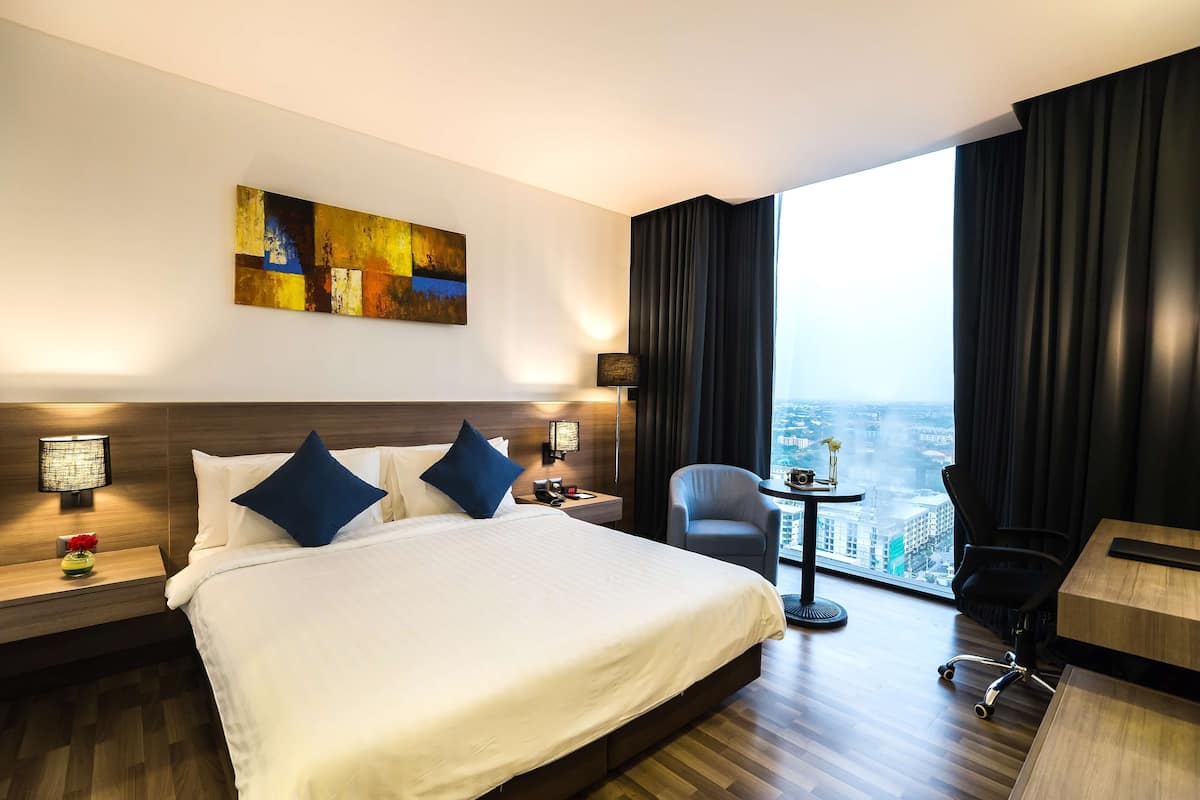 Une chambre d’hôtel avec un grand lit, un bureau, une chaise, une petite table avec un vase et une vue sur la ville.