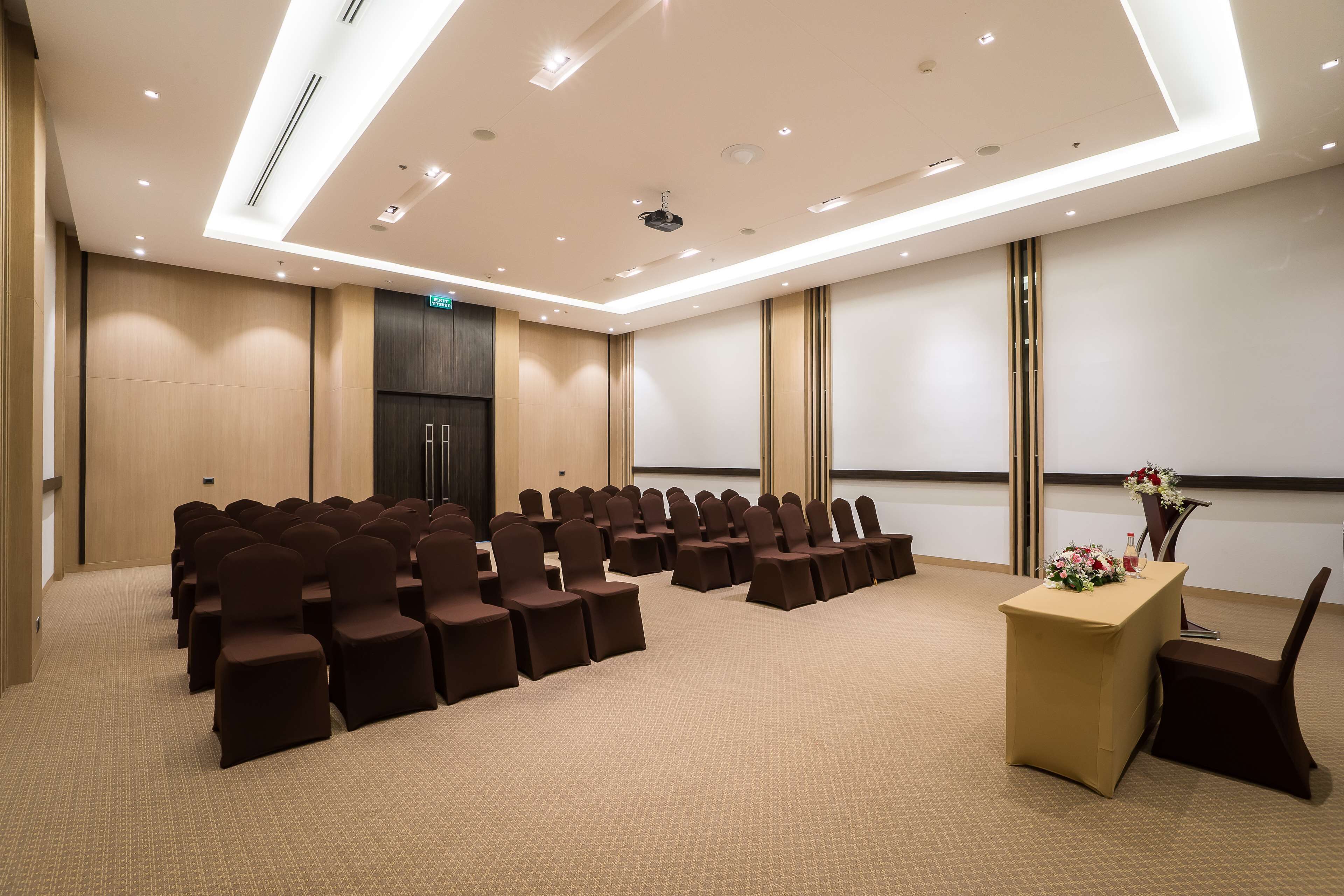 A conference room with rows of chairs, a projector screen, and a podium with flowers.