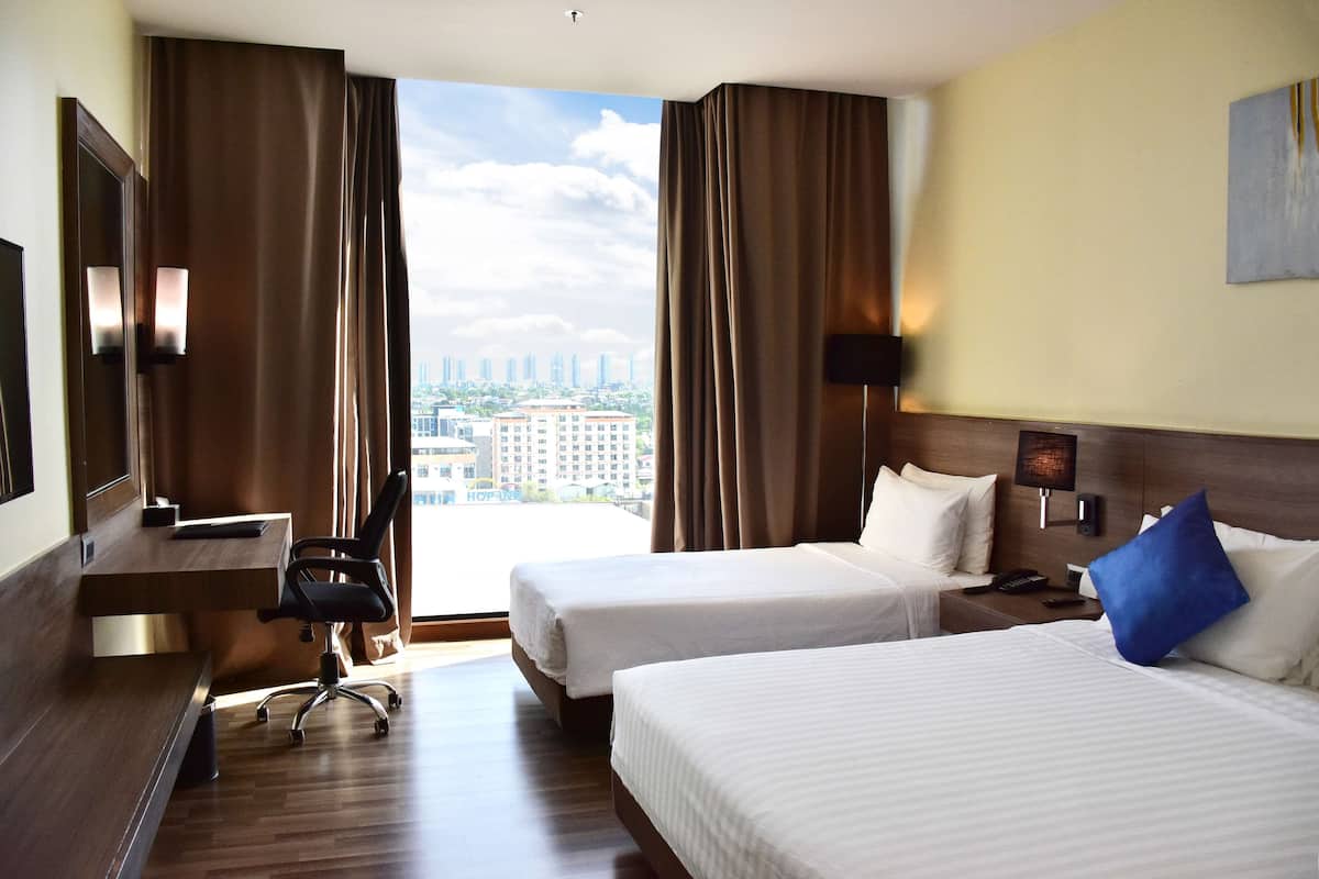 Une chambre d’hôtel avec deux lits, un bureau, une chaise et une grande fenêtre donnant sur la ville.