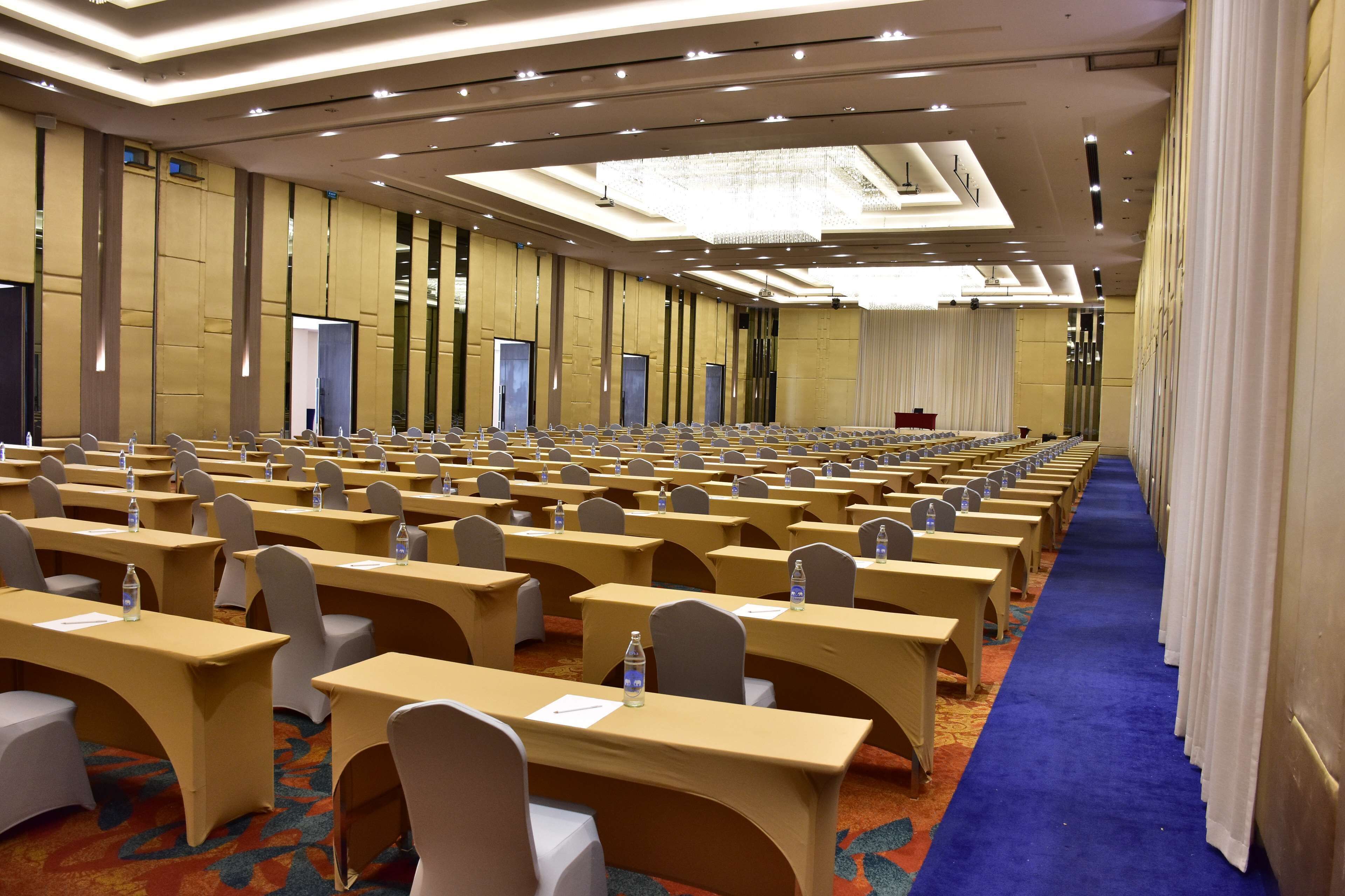 Un salón de conferencias con filas de mesas y sillas, equipado con botellas de agua y tarjetas de identificación, y una alfombra azul.