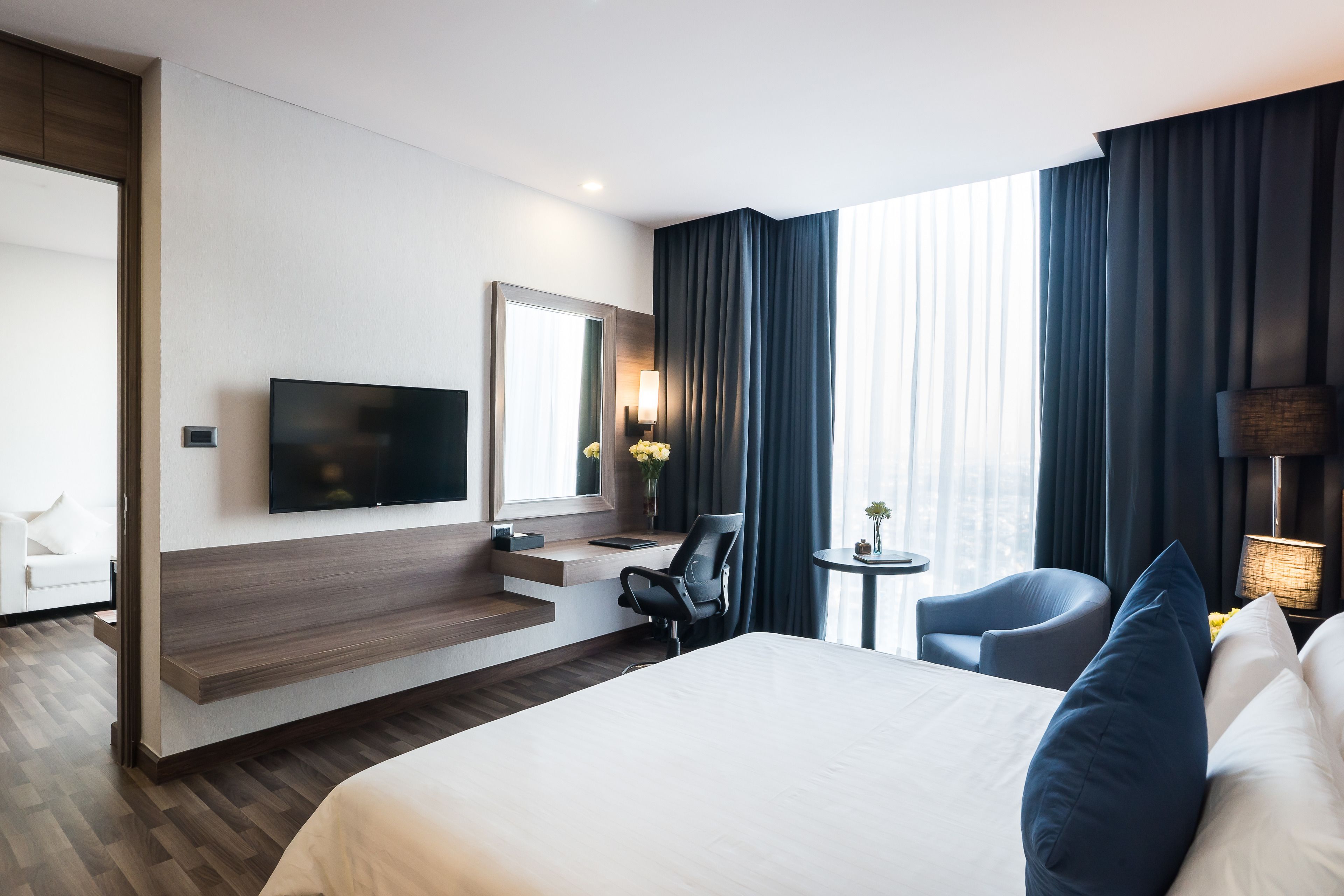 Ein modernes Hotelzimmer mit einem großen Bett, einem Schreibtisch mit Stuhl, einem Flachbildfernseher und einem großen Fenster mit Vorhängen.